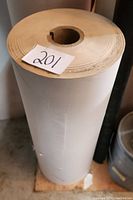 Full height view of cylindrical roll of masking paper standing on floor, showing paper wound tightly around cardboard core with a note '201'.
