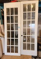 Pair of white solid wood French doors with 15 glass panes each, standing side by side, showing the full door fronts.