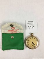 Full view of pocket watch with green and white soft pouch carrying case showing branding on interior flap.