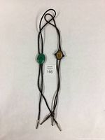 Full view of both bolo ties showing the entire length with black and brown braided cords and stone settings.