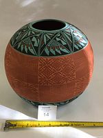 Full view of the round vase showing the carved terracotta body and painted geometric turquoise and black upper band.