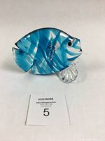 Front angled view showing the blue and teal striped body with clear glass stand and detailed eyes.