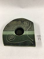 Top view of irregular shaped ceramic flower frog with a center hole containing metal pins and green glazes with spiral slip trail decoration.