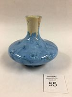 Full view of the vase showing the bulbous body, narrow neck, cream-colored neck with blue glaze dripping down, and blue crystalline glaze on body with visible crystal formations.