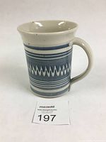 Front and side view of the ceramic mug showing cobalt blue zigzag and striped design on white background, the handle, and flared rim.
