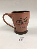 Left side view showing the bicycle image and 'YES' text on the handmade ceramic mug with pink and brown glazing.