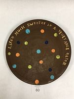 Full view of round dark brown ceramic plate with scattered colorful dots and text around the edge.