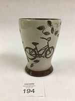Full view of tumbler showing brown bicycle and leaf design against beige background with flared base.