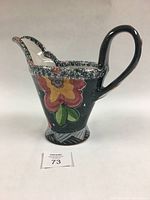 Front angle of Graeme Allemeersch majolica jug showcasing floral motif on black background, speckled rim and large handle.