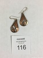 Photo showing both earrings laid flat, displaying teardrop shape and dragonfly designs with seller auction number tag