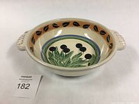 Oval ceramic olive dish with painted olive branches and black olives, beige and black leaf border, and two handles.