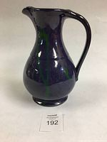 Purple ceramic jug angled to show handle and body with green drip glaze accents.