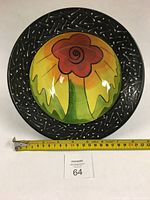 Top view of the round porcelain bowl with floral underglaze design and black rim with white slip decoration, including tape measure showing size.