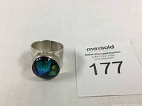 Sterling and fused glass ring next to an auction number card.