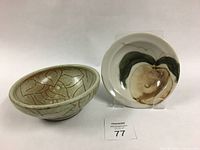 Two small ceramic bowls displayed on white surface; one bowl tan with etched abstract lines, other white with brown black swirl inside.