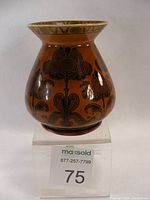 Front angled view of the antique brown ceramic Albemarle Ridgeway vase on a clear stand, showing flared rim and floral black decorations.