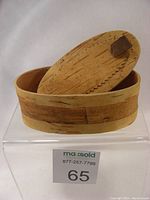 Front and slightly angled view of oval birch bark box with lid partially tilted inside box.