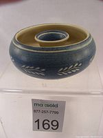 Top view of round ceramic flower frog showing central raised ring and blue glaze with white leaf pattern on sides.