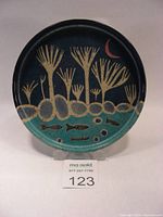 Full view of ceramic plate with land and sea motif including trees, rocks, fish, and crescent moon.