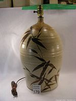 Full view of large beige ceramic lamp with brown bamboo leaf painted design and electrical cord with plug