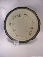 Full view of the large round serving platter with scalloped edges and floral design in the center, standing on a clear display stand.