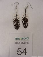 Front view of pair of hand beaded eagle feather drop earrings showing black, white, brown, and beige Miyuki Delica beads in feather pattern with fish hook style ear wires.