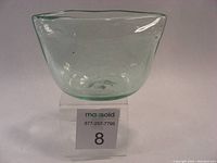 Front view of transparent blown glass vessel showing square-shaped body with irregular rim and subtle green tint.