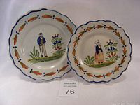 Two scalloped-edge faience plates with painted Breton peasant figures and floral patterns. Plates show slight wear with some chips.
