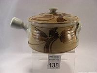 Front side view of the ceramic casserole dish and lid with visible long handle and decorative leaf design.