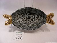 Front angle view of fish-shaped serving dish showing blue and white wave patterned interior and gold tail handles