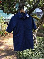 Front view of blue traditional Indonesian men's shirt on hanger outdoors, showing pattern and condition