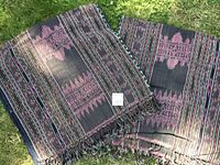 Two folded Indonesian cotton ikat blankets with traditional West Sumba patterns in dark and pink colors, fringed edges visible.
