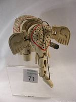 Front angled top view of white hand carved elephant marionette showing painted black and red accent details and crochet style perforations on the head