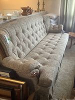 Front and side views of a four-seater sofa with tufted gray fabric and wooden trim on back and arms.
