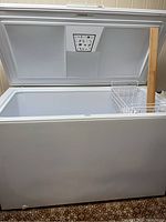 Photo showing inside of white chest freezer with open lid and three wire racks on one side plus a wooden stick inside.