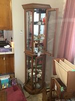 Full view of tall, narrow solid maple curio cabinet with glass doors showing interior shelves and reflective mirror back.