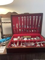 View of Community Plate silverplate cutlery in wooden case lined with red fabric showing knives, forks, spoons, some serving pieces