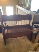 Full view of wooden bench with curved backrest and storage seat.