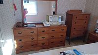 Wide shot showing the wooden dresser with 12 drawers and the tilt mirror on top; highboy dresser visible in the background.