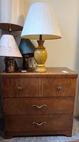 Front view of the brown wooden dresser showing three drawers with silver tone pulls and two lamps placed on top.