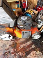 Side profile of mower showing orange deck, front and rear wheels, pull cord and bag attached