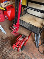 Photo of red 48-inch farm jack and red hydraulic floor jack on wooden floor near shelving.