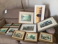 Wide view of all framed prints laid out on couch showing variety of sizes and scenes mostly by Keirstead