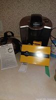 Photo showing Keurig coffee maker alongside Sunbeam kettle, instruction manual, and My K-Cup filter box.