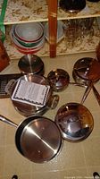 Group of stainless steel pots and lids on floor in front of cabinet