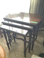 Set of three wooden nesting tables stacked together showing spindle legs and overall finish condition.