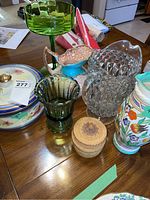 Photo showing all items arranged on table including glass stemmed dish, floral lidded bowl, green glass jug, Bursley Ware jug vase, Art Deco clear glass jug, and wicker basket