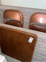 Photo showing copper-colored folding chairs partially folded behind the folding card table with a copper-colored faux leather look top.