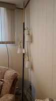 Full view of the vintage tension pole lamp positioned between wall and ceiling near window and chair.