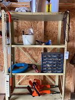 Metal shelving unit containing buckets, blue hose/coil, miscellaneous tools, and a large 28-drawer hardware caddy